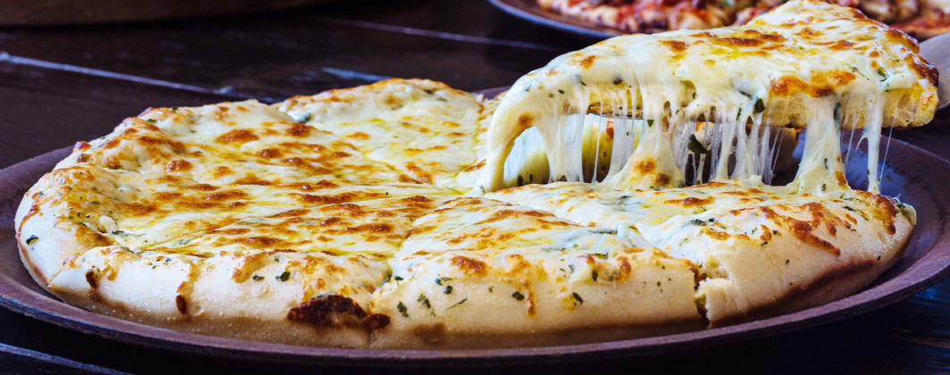 Promotional photo of a cheesy pizza. One slice is being lifted up with a paddle