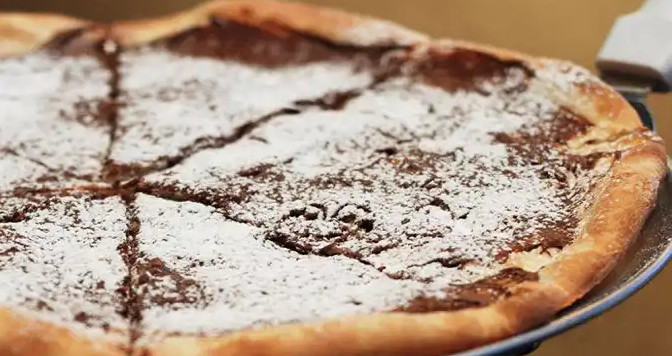 Promotional photo of a pizza covered in nutella spread and icing sugar.