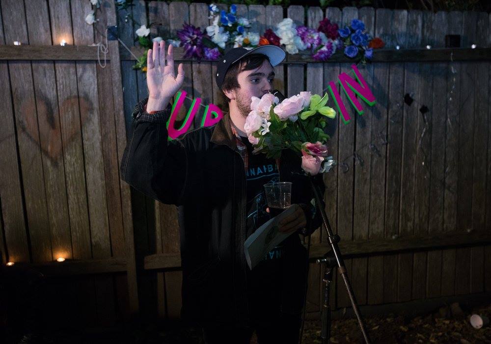 Photo of the author standing behind a microphone adorned with flowers.